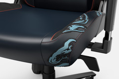 Close-up view of a gaming chair with a black seat and blue accents, featuring embroidered design on the sides. The armrest and part of the chair's back support are also visible. The chair has a modern and ergonomic design with high-quality stitching.