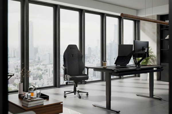 A modern office with large floor-to-ceiling windows offering a cityscape view. The setup includes a sleek black desk with dual monitors, an ergonomic chair, and a minimalist arrangement with a few accessories like a coffee cup and plant. The space is filled with natural light.