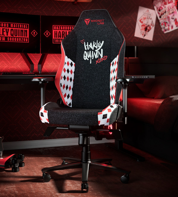A black and white gaming chair with a Harley Quinn theme, featuring the words 'Harley Quinn' in white letters on the backrest along with red 'Xoxo' and diamond patterns. The chair is placed in a room with Harley Quinn posters and a dark color scheme.